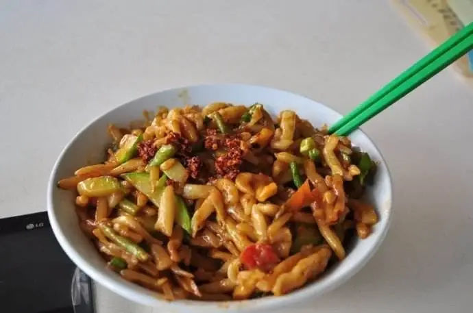 Dry-tossed cuoyuzi fish-shaped noodles with vegetables and chilli in a white bowl, chopsticks resting on the rim
