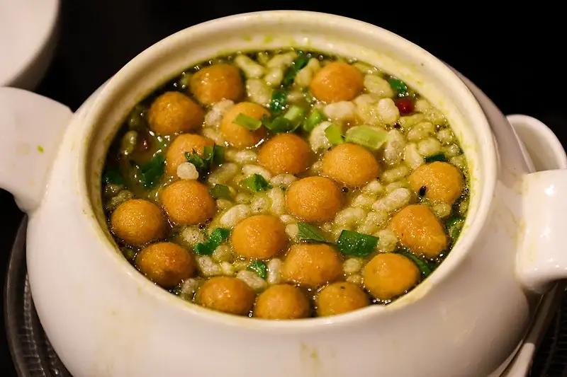 Gongcheng oil tea in a white bowl — greenish tea broth with crispy rice puffs, peanuts, scallions and fried dough balls