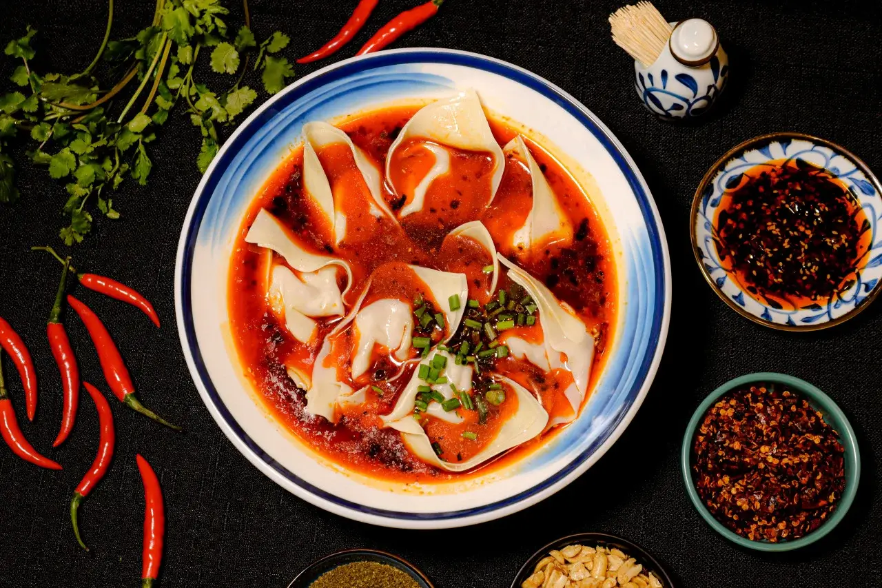 Red-oil chaoshou dumplings in a porcelain bowl with condiments around