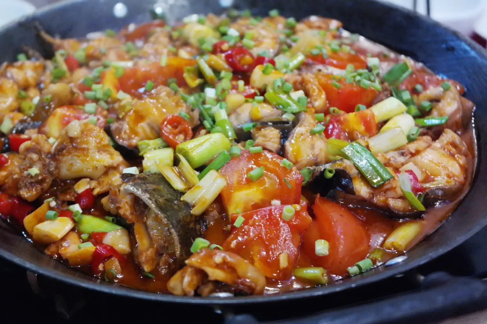 Yangshuo beer fish in an iron pan — fresh river fish cooked with beer, tomatoes, green peppers and scallions in a rich red sauce