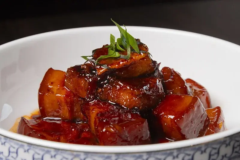 Dongpo pork braised in soy sauce with a glossy caramelised crust, garnished with scallions, served in a blue-and-white porcelain bowl
