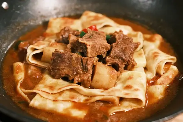 Northwest lamb stew with flatbread (huyang menbing) — tender lamb chunks and wide noodles in a rich red broth in an iron pan