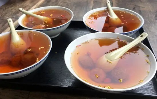 Bowls of Dunhuang apricot peel drink (xingpi shui) — amber-coloured sweet-sour beverage with dried apricots, goji berries and osmanthus flowers