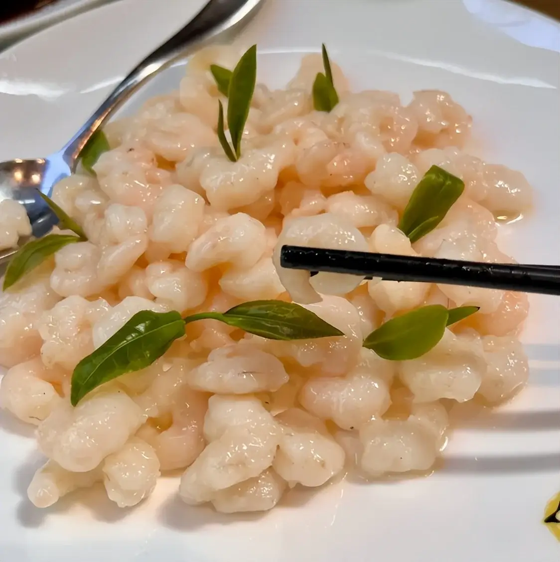 Longjing shrimp — translucent white river shrimp stir-fried with fresh green Longjing tea leaves, picked up with black chopsticks