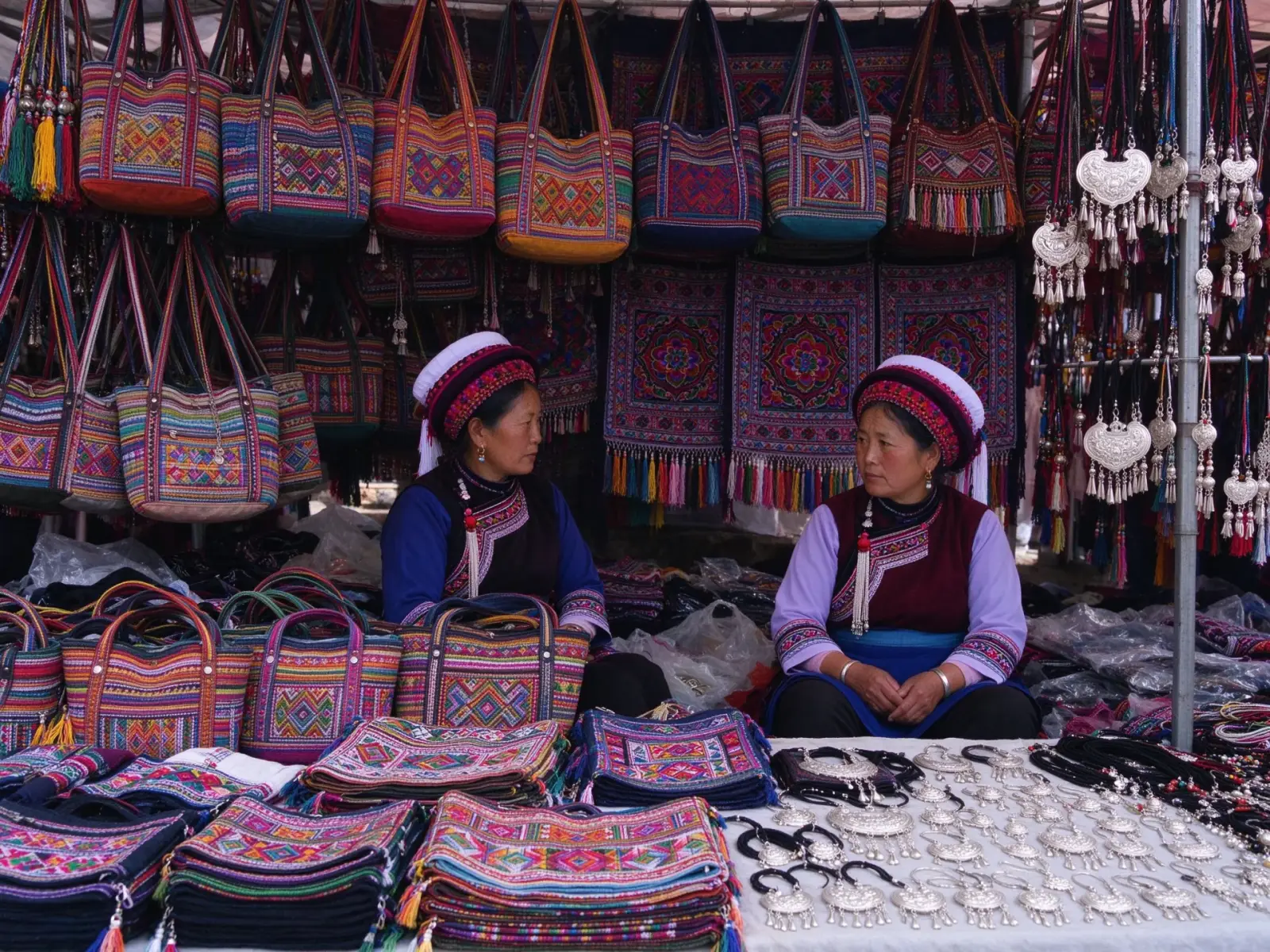 A market stall of woven bags, embroidered textiles and colourful handicrafts tended by women in ethnic dress