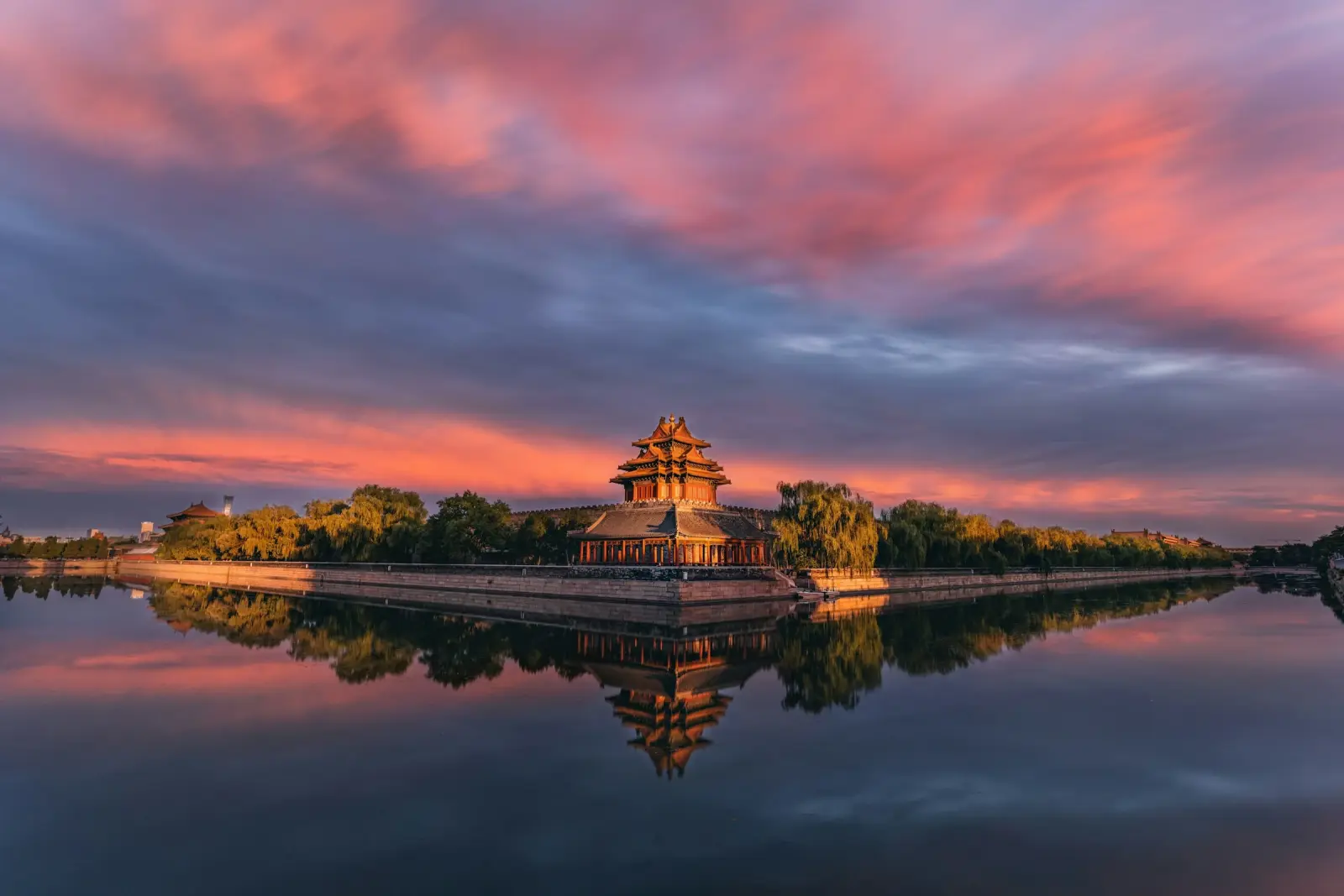 Sunset clouds reflected in the moat around a golden corner tower of the Forbidden City