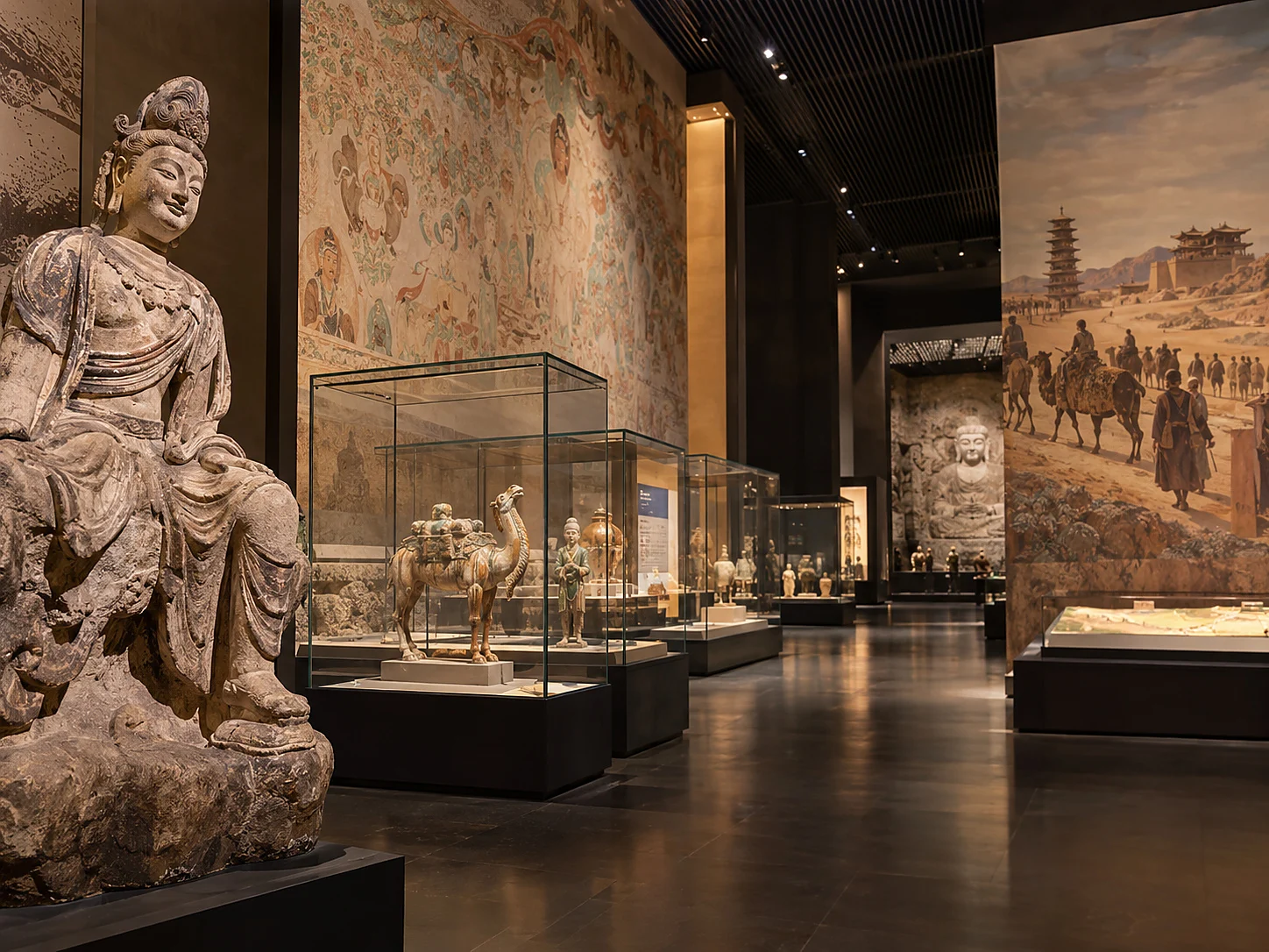 Museum gallery with a seated Bodhisattva statue, a Sogdian camel figurine and large Silk Road murals on the walls