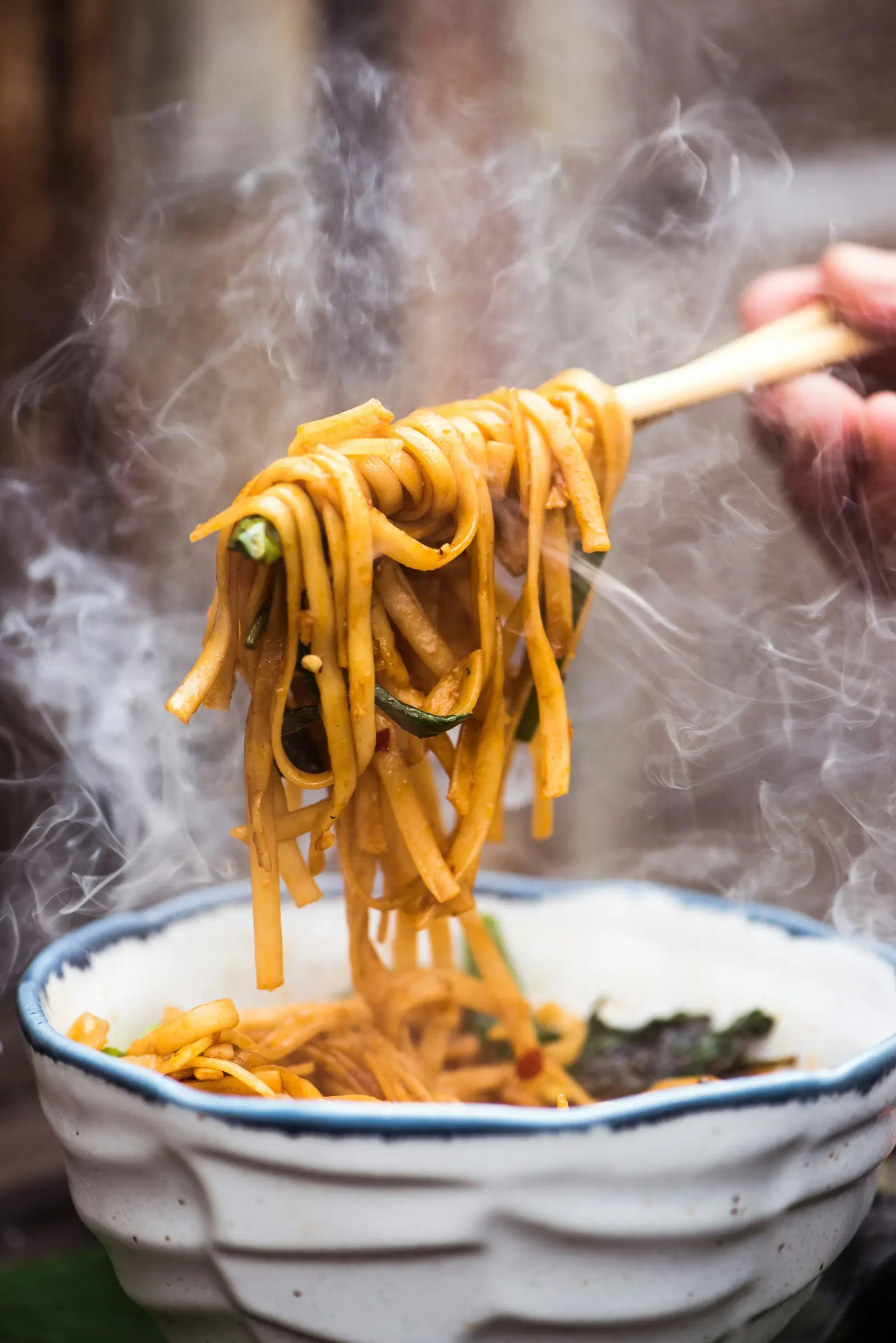Steaming Chinese noodles lifted above a ceramic bowl